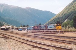 Passengers stand enjoying the warm sunshine while extra engines are added to the train.